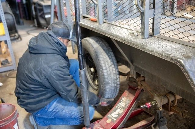 Person reparerer tilhenger ved hjulet med en jekk